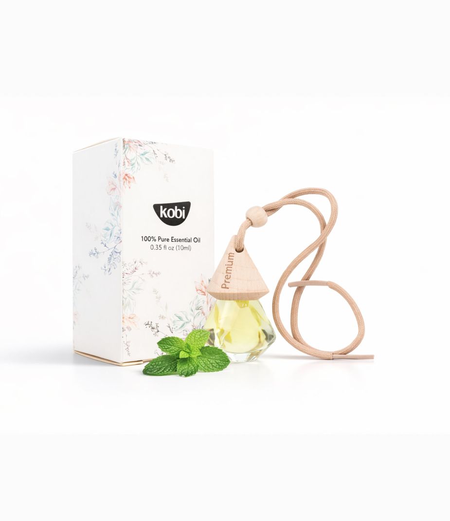 Tinh dầu treo xe ô tô Bạc Hà Kobi với hộp trắng, chai treo gỗ và lá bạc hà tươi trên nền sáng sạch