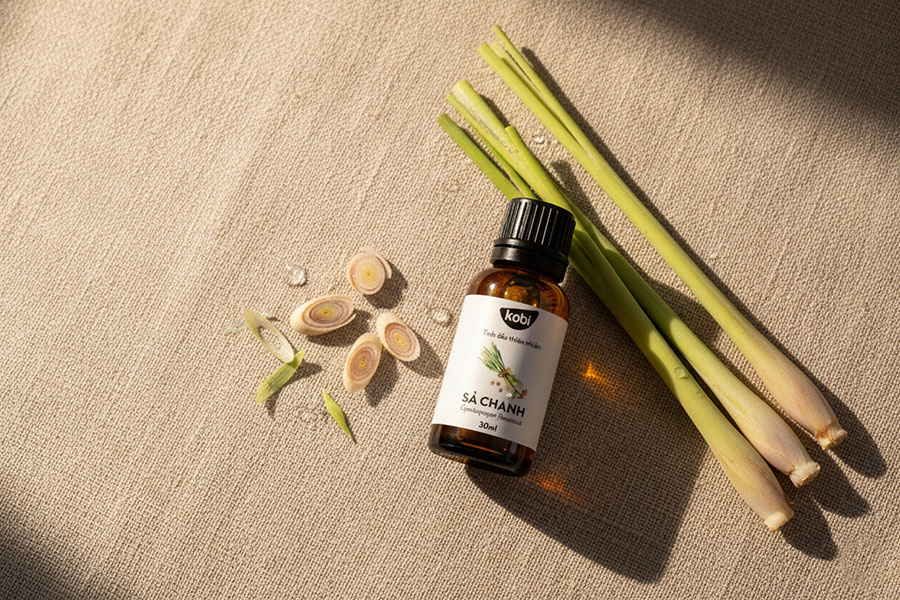 Chai tinh dầu Sả Chanh Cymbopogon citratus Kobi 30ml đặt cạnh thân sả tươi trên nền vải linen ánh sáng tự nhiên